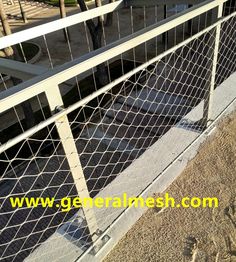 a dog is standing on the side walk near a fence and some sand in front of it