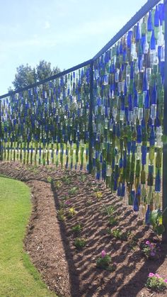 there is a fence made out of wine bottles and flowers in the ground next to it