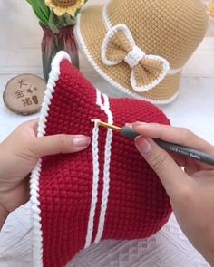 a woman is holding a red knitted pillow with a white stripe and a bow on it