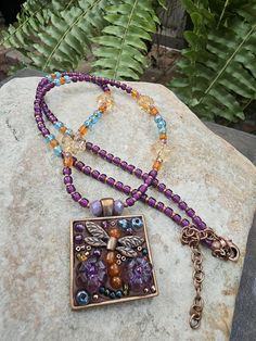 This 1.25"x1.25" stainless steel copper finish bezel features a cheery metal dragonfly with an orange glass bead body. Light purple resin flowers add a gardenlike vibe. The 20" necklace with 2" extender and lobster closure features pale orange resin flowers as well as glass beads in orange, light blue, and violet. The necklace arrives in a violet burlap bag for easy gifting or protective storage.  Each piece is a one of a kind design. I hope it brings the wearer as much joy as I had making it! Copper Beaded Necklace As Gift, Copper Beaded Necklace For Gifts, Copper Beaded Necklace For Gift, Spiritual Copper Beaded Necklaces As Gift, Handmade Bohemian Dragonfly Necklace, Bohemian Handmade Dragonfly Necklace, Spiritual Beaded Copper Necklaces, Nickel-free Copper Necklaces For Crafting, Bronze Copper Beaded Necklaces As Gifts