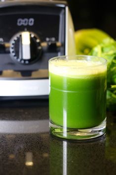 a green juice in a glass next to a blender