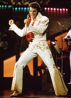 elvis presley performing on stage in white outfit with red flowered garland around his neck