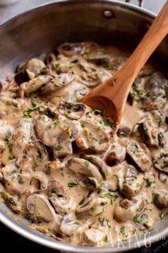 a pan filled with mushrooms and gravy next to a wooden spoon in it