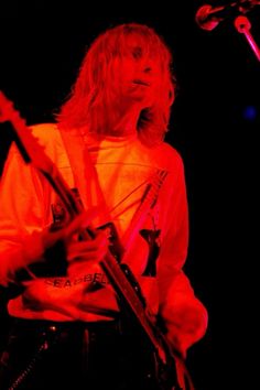 a man with long hair holding a guitar in front of a microphone and singing into a mic