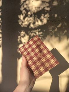 a hand holding a piece of paper with a checkered pattern on it, in front of a tree