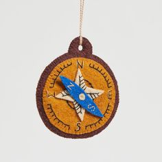 a compass ornament hanging from a string on a white wall with a blue and brown cord