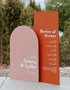 an orange and pink sign sitting on top of a cement ground next to trees in the background