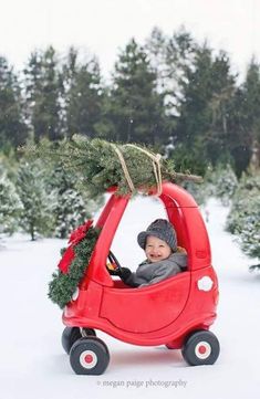 a baby in a red car with a christmas tree on top