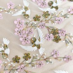 embroidered fabric with flowers and birds in pastel pink, white and gold colors on a beige background