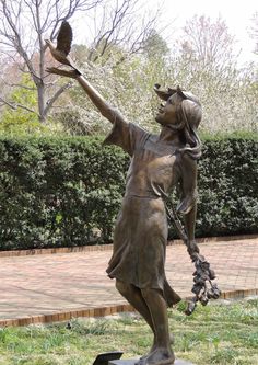 a bronze statue of a girl holding a bird in her right hand and pointing to the sky