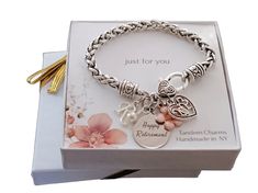 a bracelet with two charms and a heart charm on it in a box next to a tassel