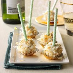 four cupcakes with green and white frosting on a plate next to a bottle of wine