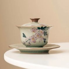 a tea cup and saucer sitting on top of a white table with pink flowers