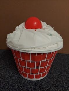 a red cupcake with white frosting and a cherry on top sitting in a container