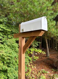 a mailbox is attached to a wooden post in front of some trees and bushes