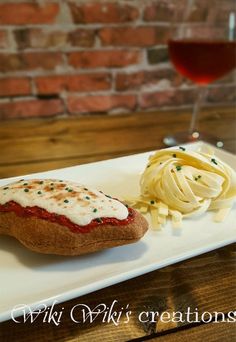 a white plate topped with pasta and sauce next to a glass of red wine on top of a wooden table