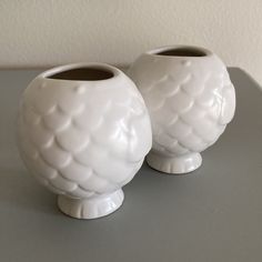 two white vases sitting on top of a gray table next to each other,