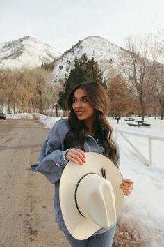 a woman is standing in the snow holding a hat