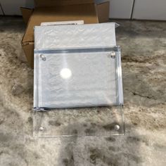 a clear acrylic box sitting on top of a carpeted floor next to a cardboard box