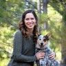 a woman standing in the woods with her dog and smiling at the camera while posing for a photo