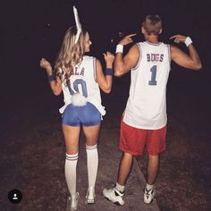 a man and woman in basketball uniforms standing on the side walk with their backs to each other