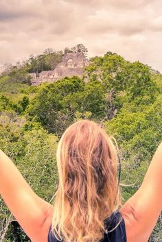 a woman standing on top of a lush green hillside with her arms in the air