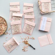 several pink packets with flowers on them next to a bowl of dried flowers and a pair of scissors