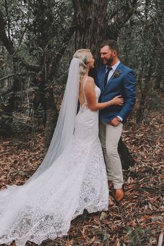 a bride and groom standing in the woods