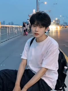 a young man sitting on the edge of a bridge