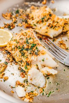 a plate with some fish on it next to a fork and lemon wedged up