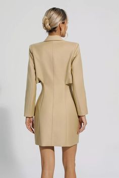 the back view of a woman wearing a beige blazer and short skirt, with her hands in her pockets