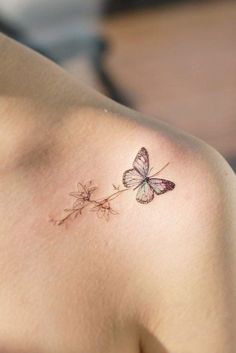 a small butterfly tattoo on the back of a woman's shoulder, with pink flowers