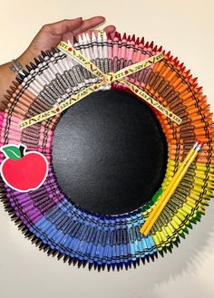 a hand holding a black circle with colored crayons and an apple on it