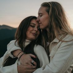 two women embracing each other in front of mountains