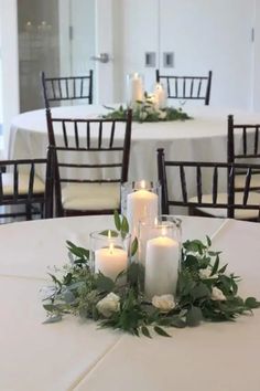 candles are lit on top of the table in front of white linens and greenery