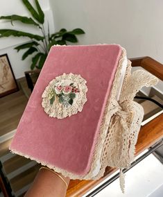 a woman holding up a pink book with lace on the cover and flowers on it