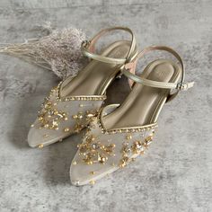 a pair of shoes with gold beading and pearls on the toes, sitting on a gray surface