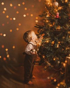 a little boy standing in front of a christmas tree with his hand on the baby's face