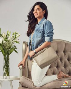 a woman sitting on a couch holding a large purse in her hand and smiling at the camera