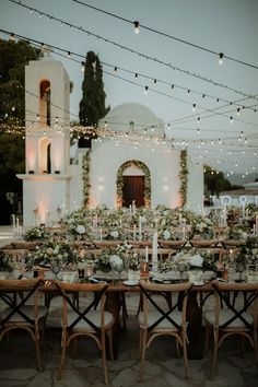 an outdoor dinner table set up with candles, flowers and greenery in front of a church