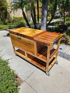 a large wooden cart sitting on top of a sidewalk next to a tree and bushes