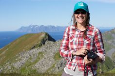 a woman standing on top of a mountain holding a camera