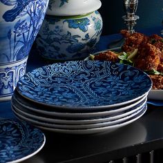 a table topped with plates covered in blue and white dishes next to vases filled with flowers