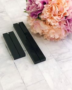 two pieces of black plastic sitting on top of a white marble floor next to a bouquet of flowers