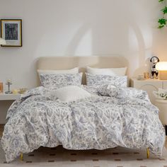 a bed with white and blue comforters in a room next to a table, lamp and pictures on the wall