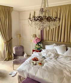 a fancy bedroom with chandelier, bed, and two chairs in the corner