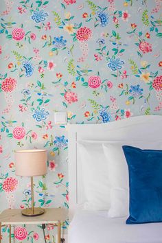 a white bed sitting next to a blue and pink wallpaper covered in floral designs