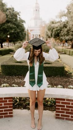 a young woman wearing a green and white graduation cap standing in front of a brick wall