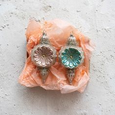 two ornaments sitting on top of an orange piece of paper next to a white wall