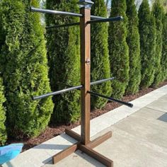 a wooden rack with three bars in front of some bushes and a blue wheelbarrow